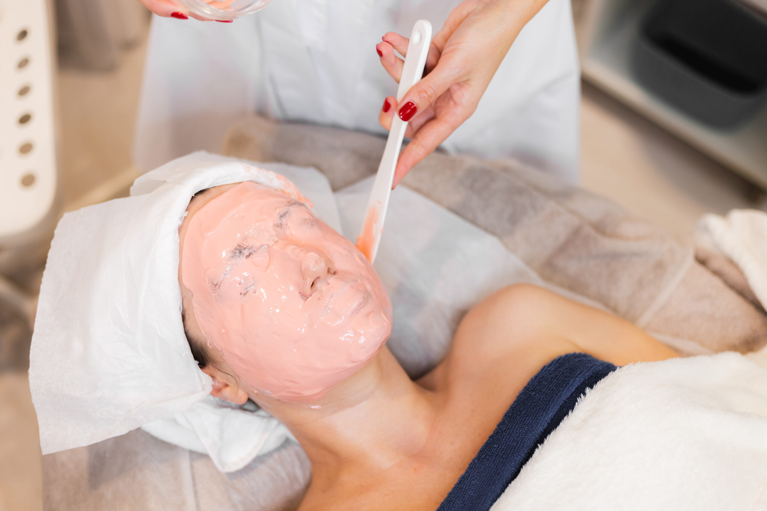 Cosmetologist applies alginate mask with spatula on face of woman. Facial skin and anti-aging treatment. Cosmetology and professional facial skin care.